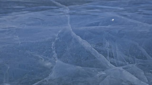 Snow is flying over surface of ice. Snowflakes fly on ice of Lake Baikal. Ice is very beautiful with unusual unique cracks. Snow sparkles and glows in red. Shooting slow motion 180fps. Picture at