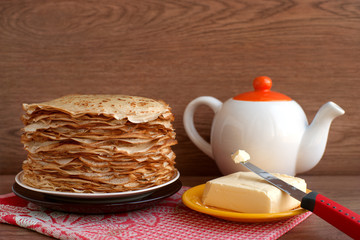 Pancakes with butter. Maslenitsa. Pancakes with butter and tea on a wooden background. A large stack of thin pancakes with a crispy crust. Knife cut the butter for pancakes.