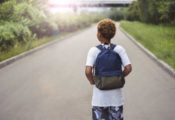 Portrait of the cute african american boy who is going to school with his school  backpack. Student mixed boy on his way to the school. Study for children. Road. Shooting on the july 2018.  - Powered by Adobe