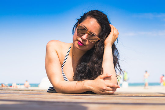 Woman with sunglasses lying on the wooden boardwalk on the beach