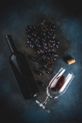 Red wine bottle with glass and grapes, dark background copy space top view selective focus