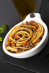 Pasta with bolognese sauce. In a white frying pan. The background is black. Italian food.
