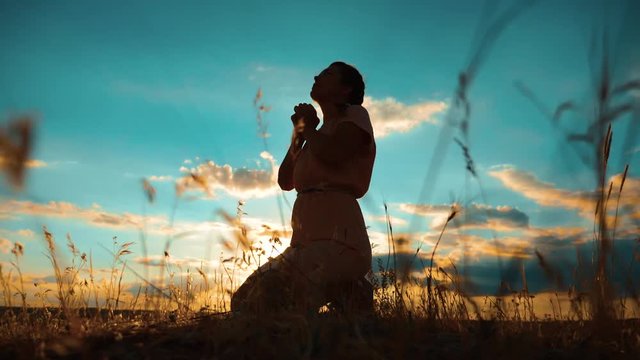 woman praying on her knees. Girl folded her hands in prayer silhouette at sunset. slow motion video. Girl folded her hands in prayer pray to God. the girl praying asks forgiveness for sins lifestyle