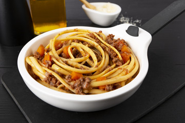 Pasta with bolognese sauce. Parmesan and olive oil. In a white frying pan. The background is black. Italian food.
