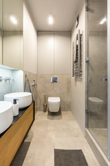 Fototapeta na wymiar White toilet under light in modern beige bathroom interior with mirror above washbasin. Real photo