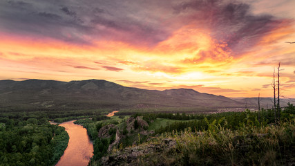 A very bright sunset in the mountains at the bottom runs a river of Khakassia