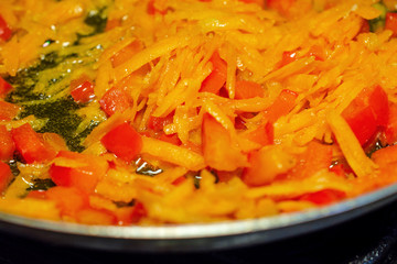 Juicy sliced bell sweet red pepper and grated carrots fried on a frying pan in olive oil. Healthy homemade vegetarian food.