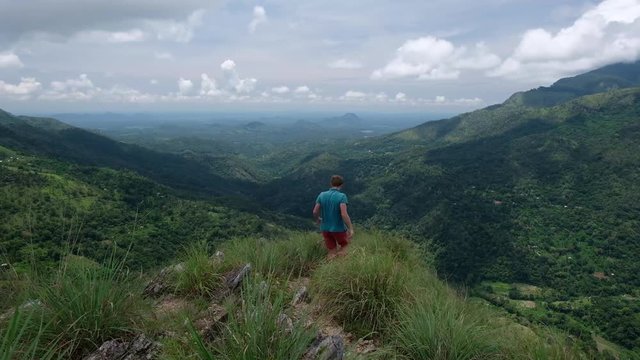 Traveler Man walking on mountains and coming to the edge of hill. View from mini Adams peak in Ella Sri Lanka