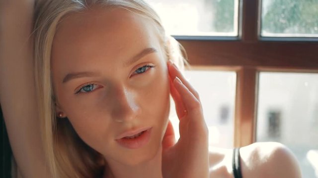 fashion portrait of a beautiful young woman with blue eyes and blonde hair poses near the window