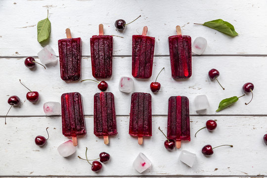 Homemade cherry ice lollies, ice cubes and cherries on white wood