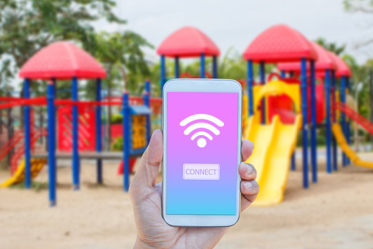 Hand holding smartphone with wifi connect on screen over outdoor play park blurred background