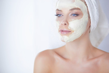 happy woman with a towel on her head puts on face mask