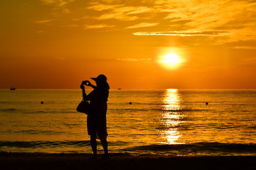 Silhouette of a woman photographing a beautiful sea in golden light. Amazing beach sunset with endless horizon