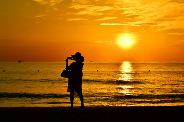 Fototapeta premium Silhouette of a woman photographing a beautiful sea in golden light. Amazing beach sunset with endless horizon