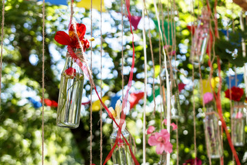 floral decoration in the form of glass mini-vases and bouquets of wildflowers hanging from above. Flower vases from bottles with bouquets of colorful flowers. Beautiful decor for the wedding ceremony