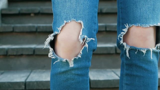 Knees of a girl in torn blue jeans. Teenager and fashion. Clothes for young people. Stylish denim pants with holes