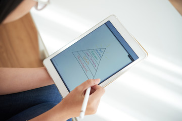 Crop view of woman in glasses drawing with pen colorful hierarchy of needs on tablet in hands...
