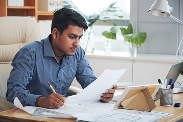 Indian adult man sitting at workplace in office and working with papers