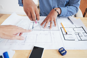 Crop hand of chief pointing at blueprint of unrecognizable Indian employee in office