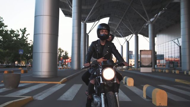 Young couple in helmets riding on motorcycle in city during sunset, slow motion