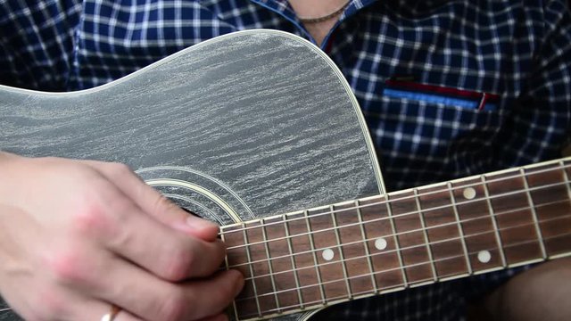 A guy in a blue checkered shirt is playing a close-up guitar