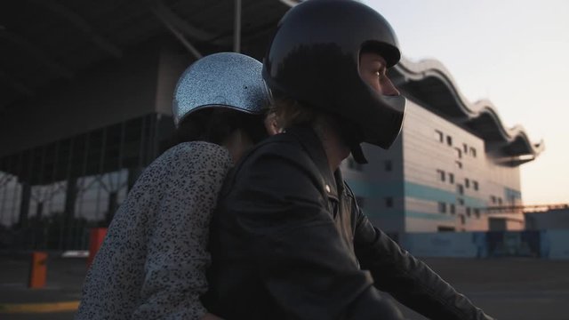 Young couple in helmets riding on motorcycle in city during sunset, slow motion, close up