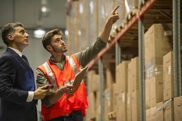 Worker and businessman with digital tablet and clipboard in warehouse