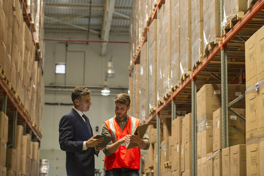 Worker and businessman with digital tablet and clipboard in warehouse