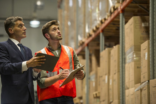 Worker and businessman with digital tablet and clipboard in warehouse