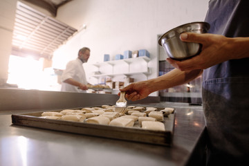Baker with brush prepares rolls for baking