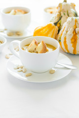 Two cups with fresh pumpkin cream soup decorated cream, seeds and crackers on white table cloth