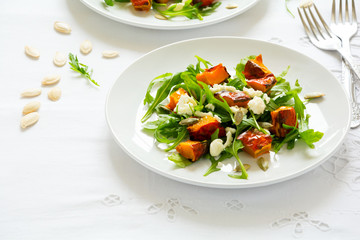 Fresh autumn salad with baked pumpkin, arugula, cheese and seeds on white table cloth. Space for copy