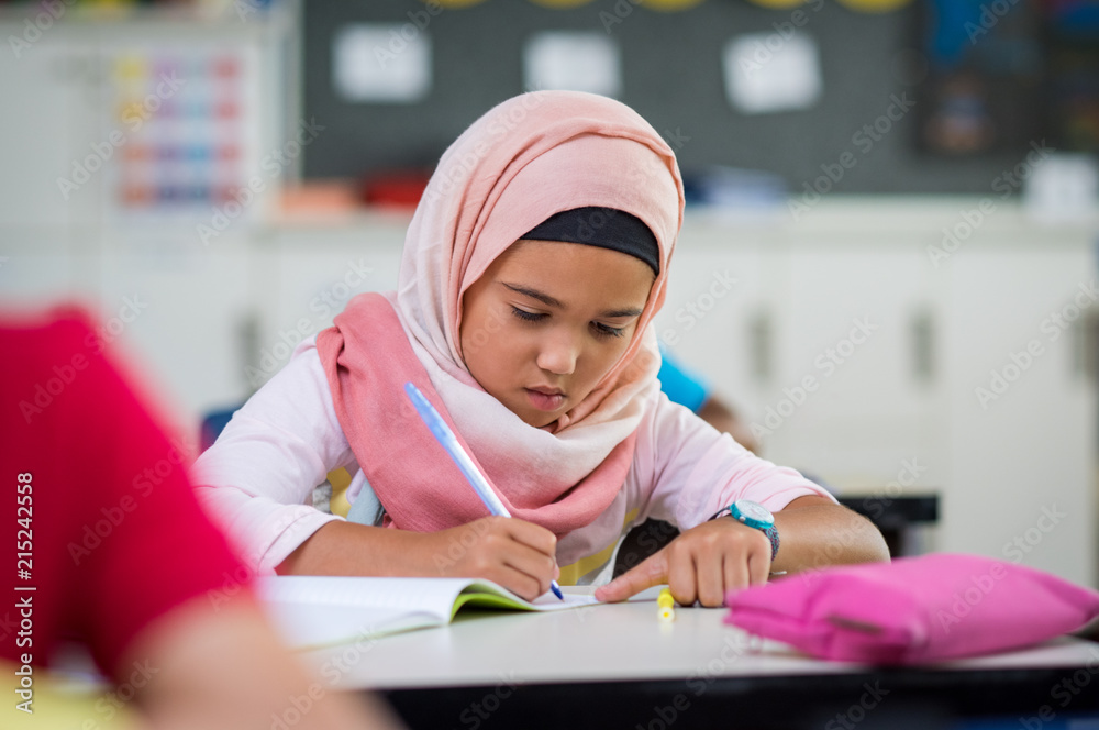 Wall mural young girl wearing hijab studying