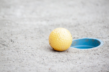 Golf ball orange color next to golf hole sand field.