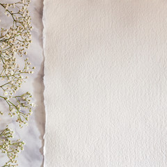 A square photo of white handmade paper on a marble table with white flowers on the left