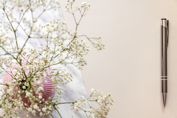 Cream elegant empty paper on a marble table with a pink vase with white small flowers
