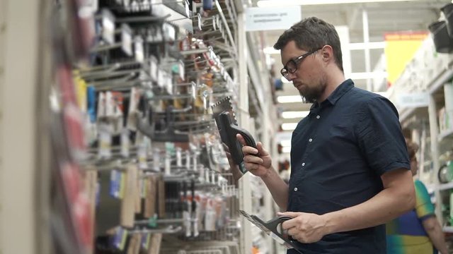 Male customer wants to buy new building spatula in a hardware store. Variety of building tools. Man choosing between two tools.