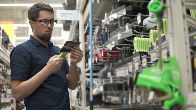 Customer choosing between wide and regular building spatula in the store. Man buying tools for house renovation. Shopping in a hardware store.