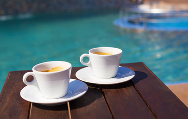 Two cups of coffee on the table near the pool.