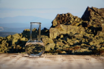 Clean water in a glass laboratory flask on wooden table on mountain background. Ecological concept, the test of purity and quality of water.