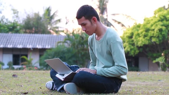 Education Learning Studying concept : Asian Boy students sitting for enjoy  searching, social with laptop for preparing final test exam at green grass in public park on vacation time in summer day.