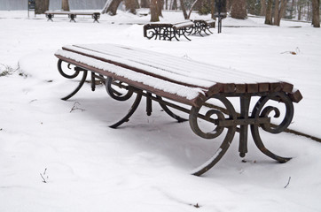 A bench in a winter park covered with snow on a winter day