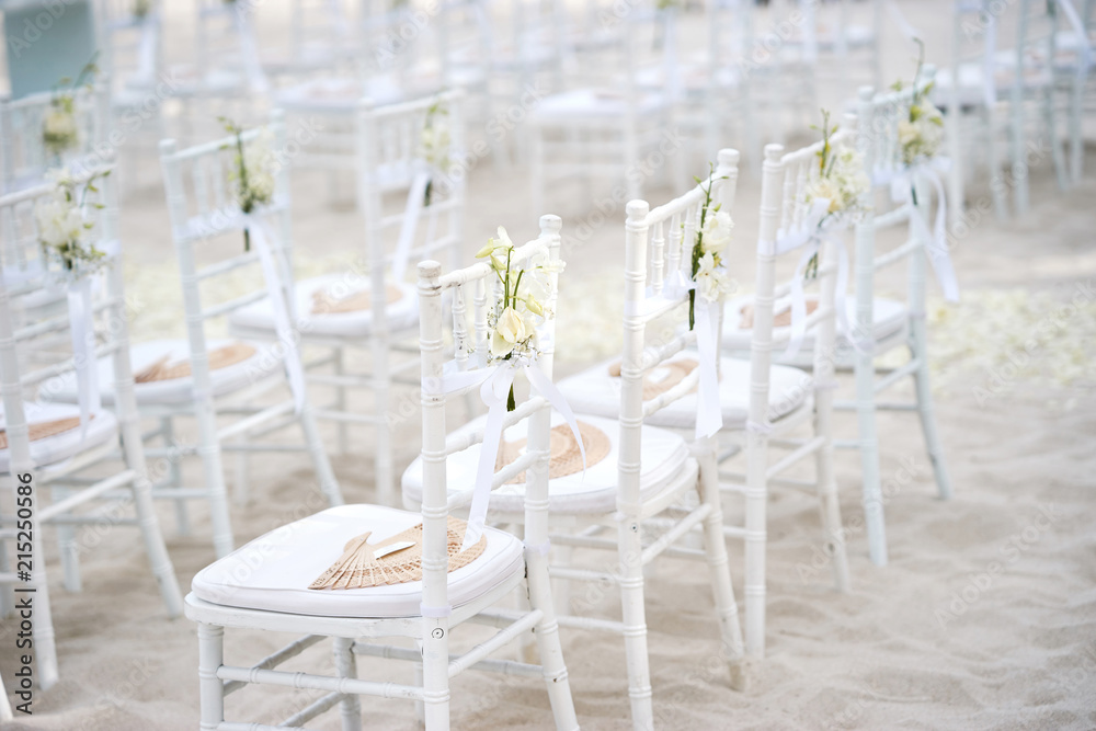 Wall mural Side view of white chiavari chairs, wedding chairs arrangement for beach wedding venue on the white sand outdoors, White ribbin with rose flower flower deoration