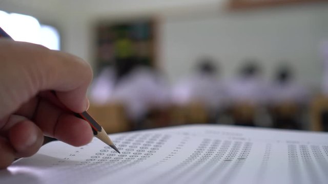 Education test concept : Hands student holding pen for testing exams writing answer sheet or exercise for taking fill in exam carbon paper computer on wood table at classroom in high school