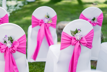 Wedding chairs, spandex white cover chairs, pink organza sash with cone of flower petals decoration setup for outdoor wedding on the green grass