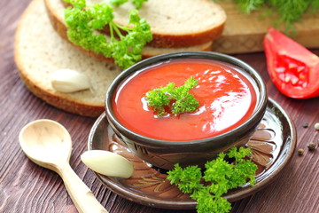 Delicious tomato soup with aromatic spices and greens on a wooden table.