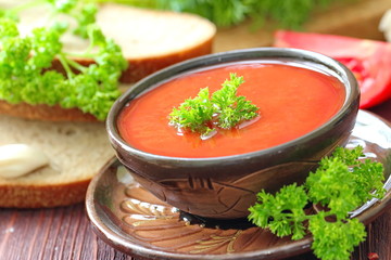 Delicious tomato soup with aromatic spices and greens on a wooden table.