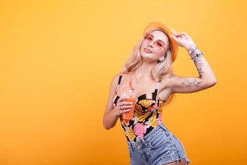 beautiful young woman with glasses holding fresh orange juice over yellow background in studio