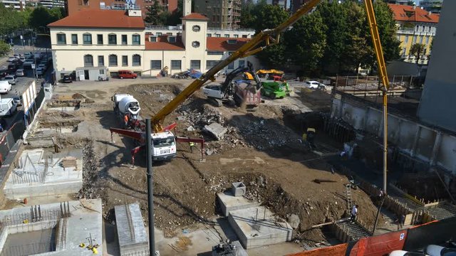 Aerial view of time lapse of a busy construction area, including laying foundations, manual workers, machinery, cranes and pouring cement - construction site concept