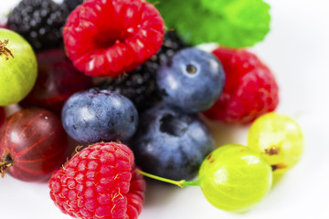Close-up arrangement mixed, assorted berries including blackberries, strawberry, blueberry, raspberries and fresh leaf on white